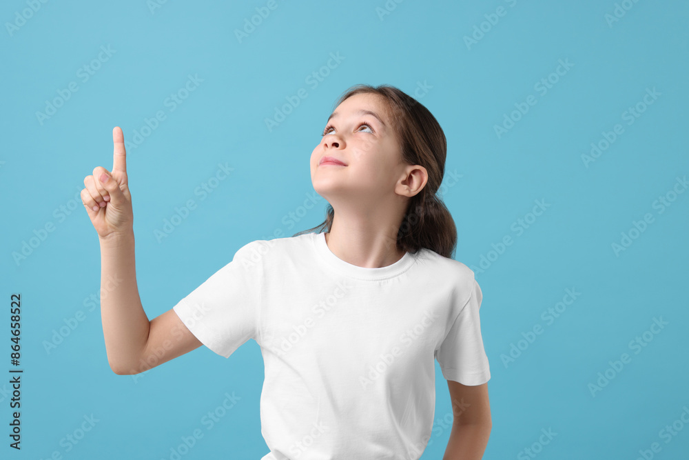 Beautiful girl pointing at something on light blue background Beautiful girl pointing at something on light blue background