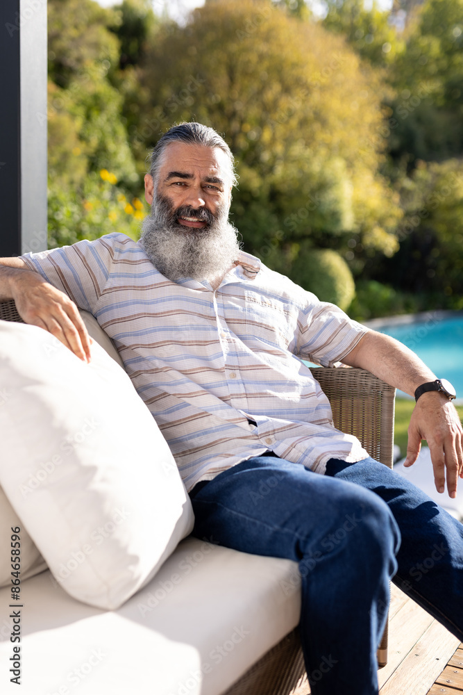 Fototapeta premium Relaxing outdoors, senior man sitting on patio sofa by swimming pool