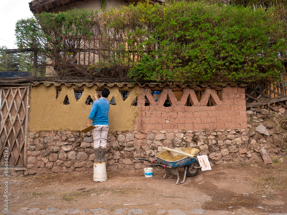 Man Wearing black Boots is Standing Over a Bucket of Paint and is Renovating an Adobe Wall