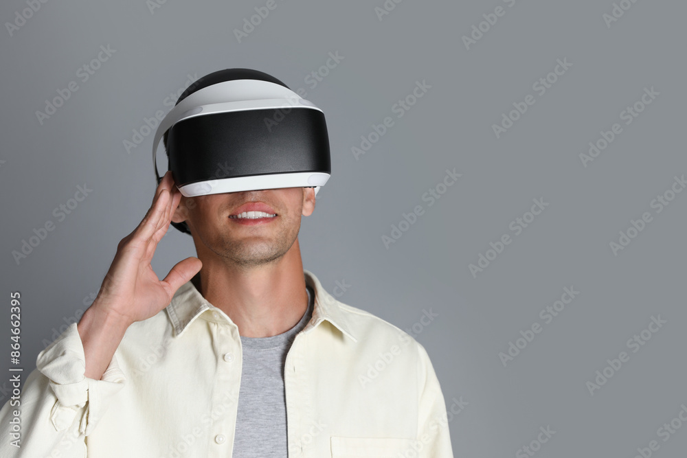Smiling man using virtual reality headset on gray background, space for text Smiling man using virtual reality headset on gray background, space for text