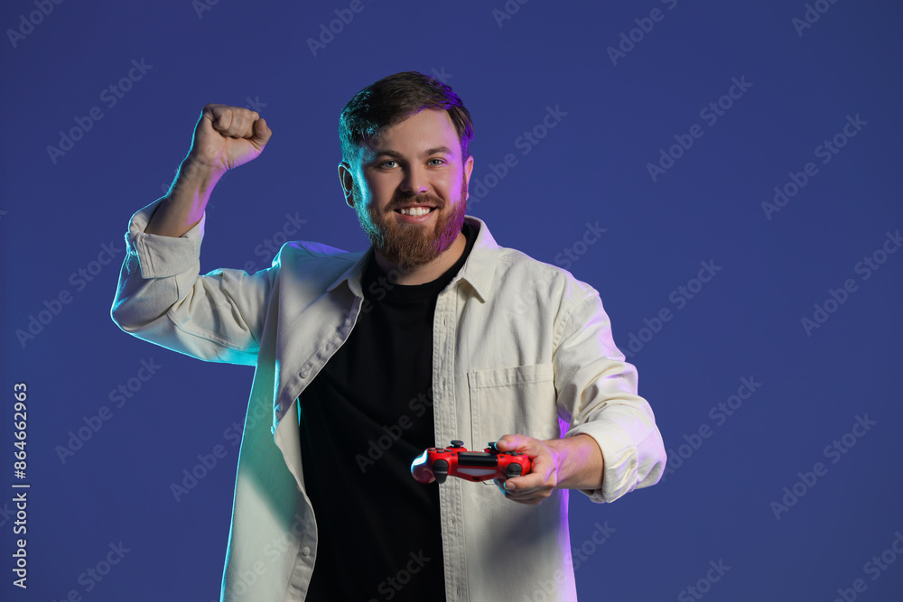 Fototapeta premium Happy man with game controller on dark blue background