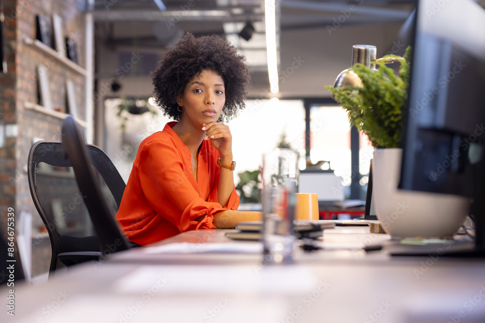 Sitting at desk, businesswoman in orange shirt looking at camera in office Sitting at desk, businesswoman in orange shirt looking at camera in office