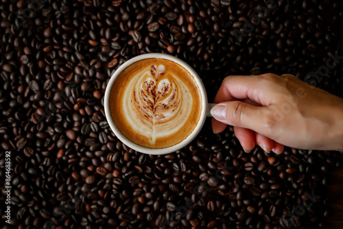 Woman hand holding coffee cup, hot latte  on coffee beans background.