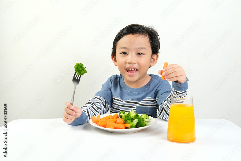 A cheerful boy enjoys a nutritious meal of steamed broccoli and carrots with a glass of orange juice. Ideal for promoting healthy eating habits, children's nutrition, and family-friendly meal ideas. A cheerful boy enjoys a nutritious meal of steamed broccoli and carrots with a glass of orange juice. Ideal for promoting healthy eating habits, children's nutrition, and family-friendly meal ideas.
