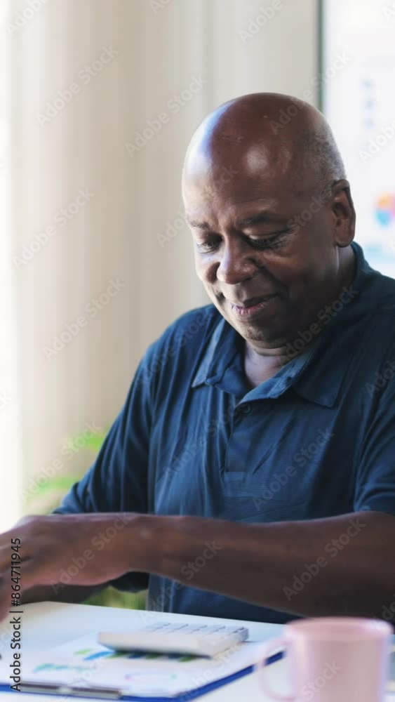 Senior African American man focused on financial documents at a desk, reviewing papers and notes. Pink mug adds a homely touch to the office environment Senior African American man focused on financial documents at a desk, reviewing papers and notes. Pink mug adds a homely touch to the office environment