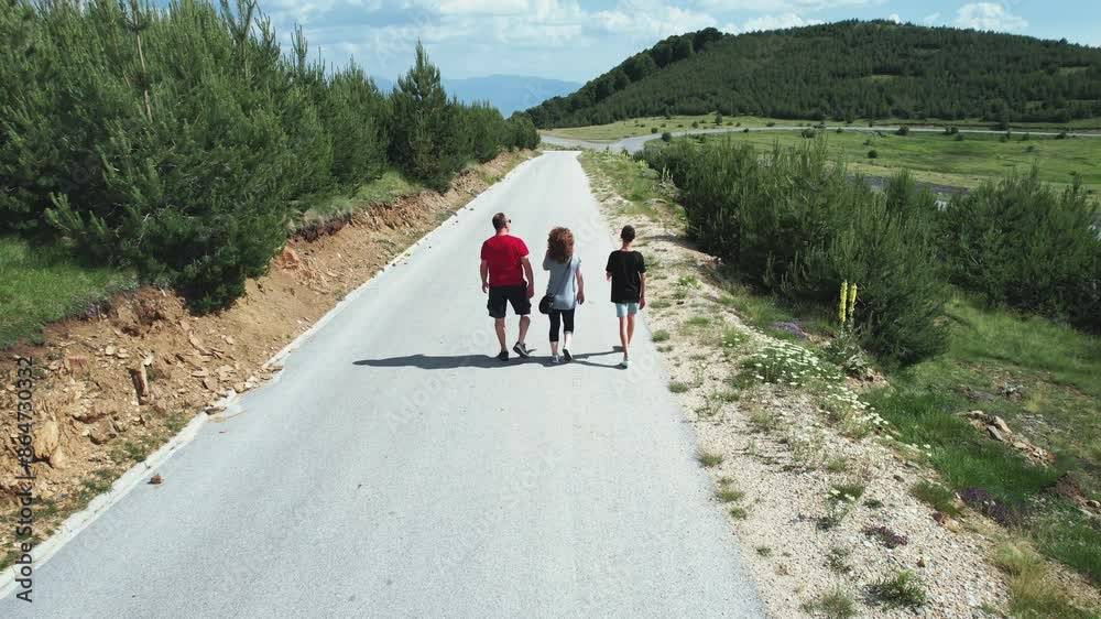 Family of three people walking hiking down a rural mountain road, aerial view Family of three people walking hiking down a rural mountain road, aerial view