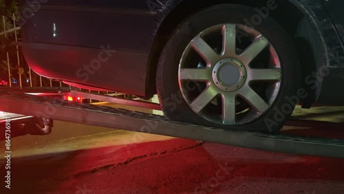 A black damaged car involved in accident is being towed by a tow truck ramp