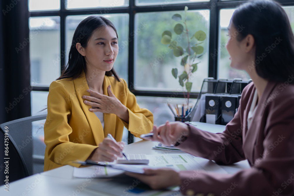 A professional photograph depicting two female entrepreneurs engaged in a collaborative discussion while diligently working in their corporate office environment.