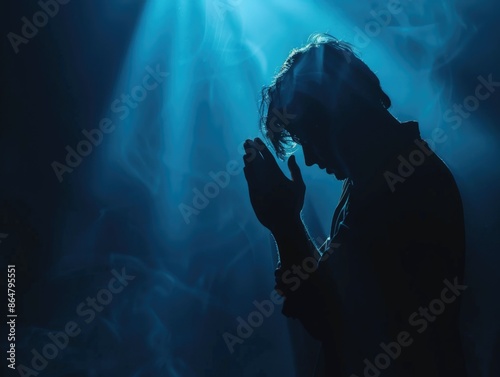 A man is praying in the dark with smoke in the background. Scene is solemn and peaceful