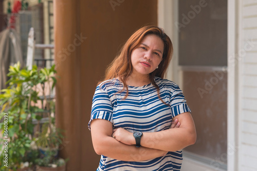 Photos An Asian woman in her 30s stands outside her apartment flat, looking at someone with a suspicious and condescending expression