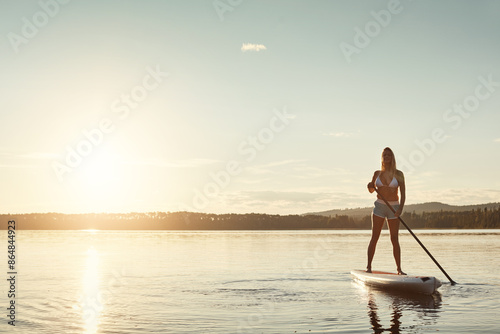 River, sunset and woman on paddle board with sunshine, water sport and vacation on lake for tourism. Exercise, summer or holiday in Germany for female person, swimsuit or travel fitness for adventure