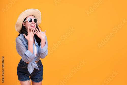 Excited Asian young woman in a sun hat and glasses to travel on holidays isolated on yellow copy space background. Travel, summer vacation, beach leisure concept.