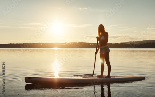 Lake, sunset and woman on paddle board for balance, water sport and vacation on river for tourism. Nature, summer or holiday in Germany for female person, swimsuit or travel exercise for adventure