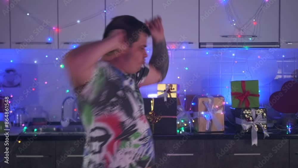 Man moving to music with raised arms at a home party decorated with multi-colored garlands, holiday lights and gifts in slow motion. Man moving to music with raised arms at a home party decorated with multi-colored garlands, holiday lights and gifts in slow motion.