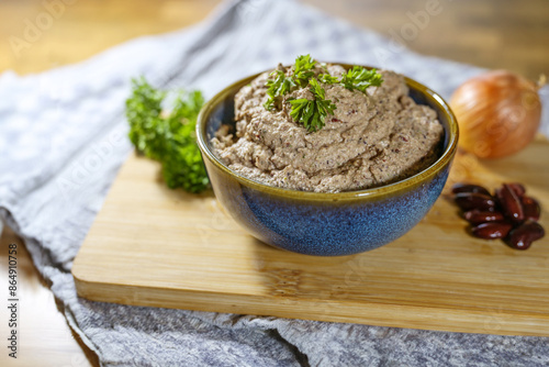 Vegan plant-based dip that is reminiscent of liver sausage, homemade from kidney beans, tofu, onion and herbs, served in a bowl with parsley garnish on a kitchen board copy space