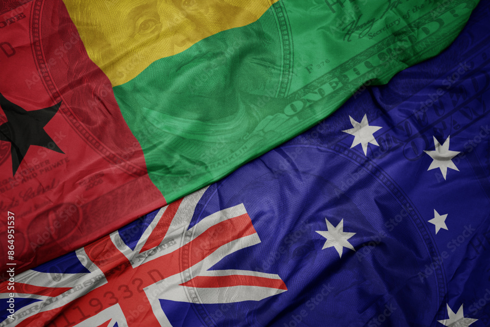 waving colorful flag of guinea bissau and national flag of australia on the dollar money background. finance concept. waving colorful flag of guinea bissau and national flag of australia on the dollar money background. finance concept.