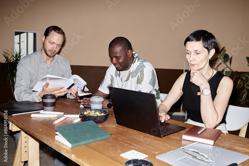 Minimal shot of business meeting with diverse group of people using computer and discussing project development in office shot with flash