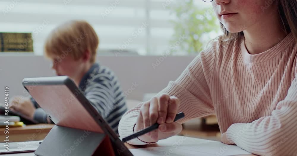 Charming Caucasian girl with dark long hair and glasses. Very attentive student sitting at desk while noting down something on tablet device. Completing activity with help of modern technology. Charming Caucasian girl with dark long hair and glasses. Very attentive student sitting at desk while noting down something on tablet device. Completing activity with help of modern technology.