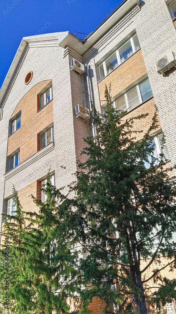 Fototapeta premium Multi-story residential building. Sale rental apartments. Housing development. City life. Real estate. Mortgage concept. Condos. Interest Rate. Flat. Green tree. Air conditioner on brick wall.