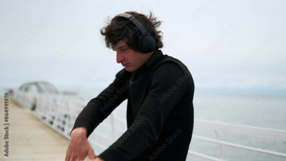 Attractive young man is dancing on foggy pier, moving to the rhythm of music with headphones, dressed in a stylish black turtleneck, listening to his favorite track. Attractive young man is dancing on foggy pier, moving to the rhythm of music with headphones, dressed in a stylish black turtleneck, listening to his favorite track.