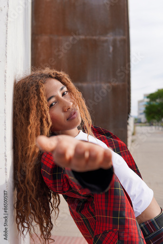 Curly haired woman wearing red checked blazer gesturing and leaning on wall photo