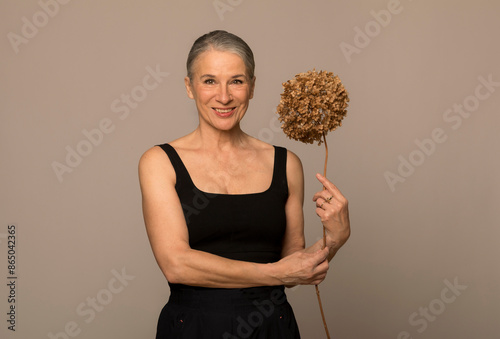 Smiling senior woman holding withered flower in front of brown background photo