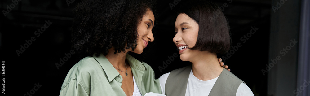 Two women, dressed in business attire, look at each other lovingly in an office setting. Two women, dressed in business attire, look at each other lovingly in an office setting.