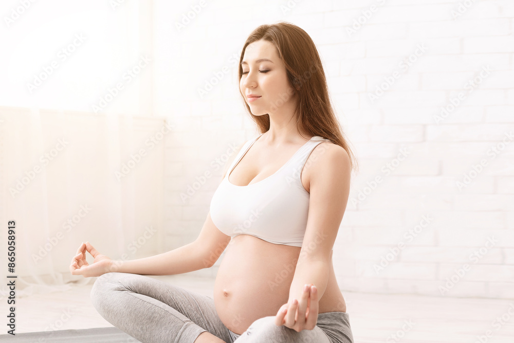 Pregnant woman doing yoga, practising padmasana in lotus position, copy space Pregnant woman doing yoga, practising padmasana in lotus position, copy space