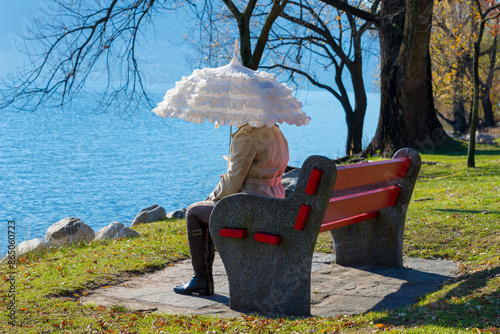 Woman with a Parasol Sitting on a Bench on the Waterfront to Lake Maggiore in a Sunny Day in Locarno, Ticino, Switzerland.