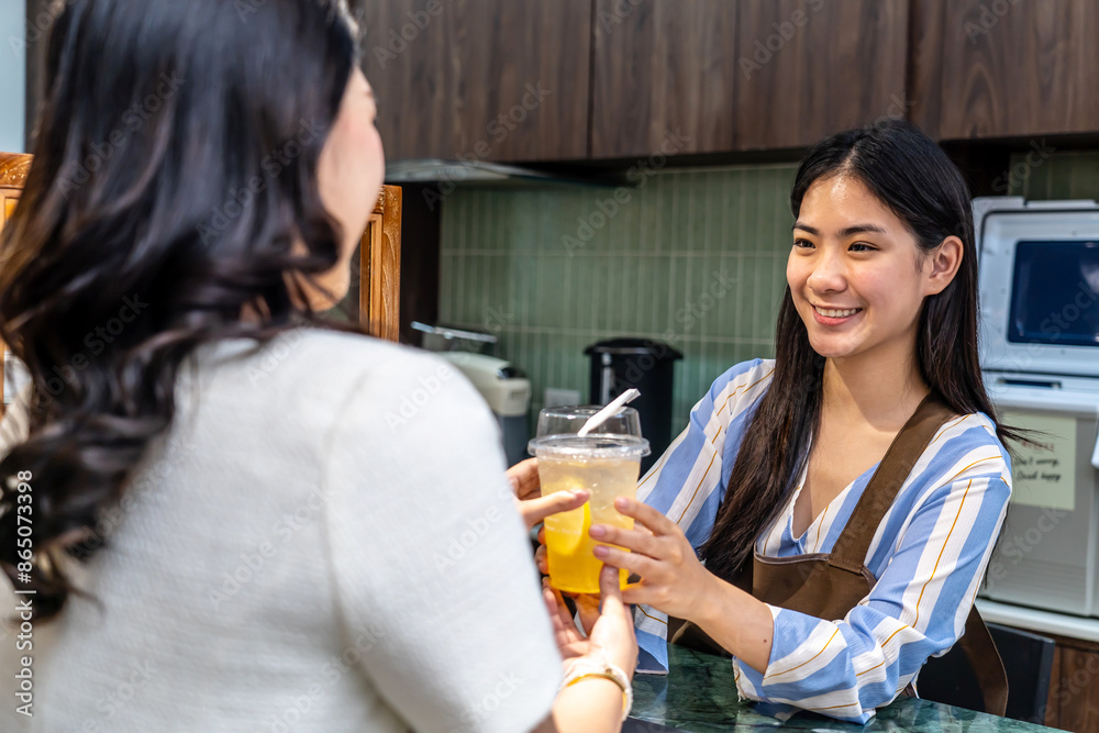 Smiling young asian waitress in a cafe with customer for service, payment or order on counter at coffee shop. Serving, employee in small business restaurant helping a girl client at checkout or work Smiling young asian waitress in a cafe with customer for service, payment or order on counter at coffee shop. Serving, employee in small business restaurant helping a girl client at checkout or work