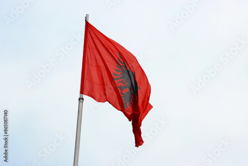 Waving flag of Albania isolated on sky background. Albanian textile flag on independence day. The symbol of the state flying on the flagpole on the cloudy sky. Copy space. photo