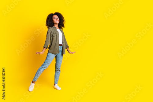 Full size photo of gorgeous girl dressed khaki jacket jeans pants dancing near at promo empty space isolated on yellow color background