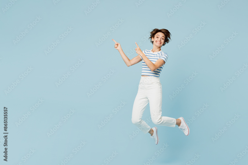 Full body young fun woman wears striped t-shirt casual clothes jump high point index finger aside on area mockup isolated on plain pastel light blue cyan background studio portrait. Lifestyle concept.