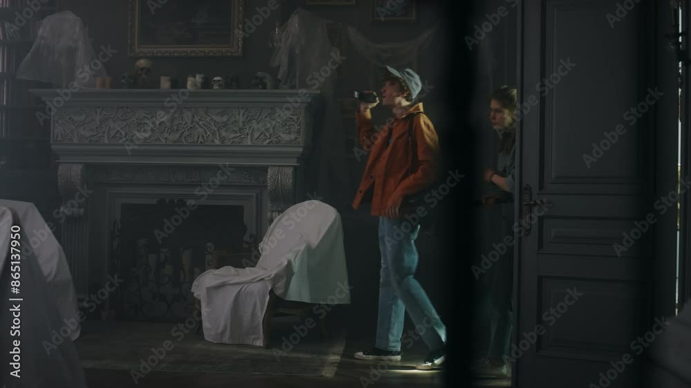 Side full shot of group of curious adolescents entering dark living room of derelict mansion and exploring it using flashlights