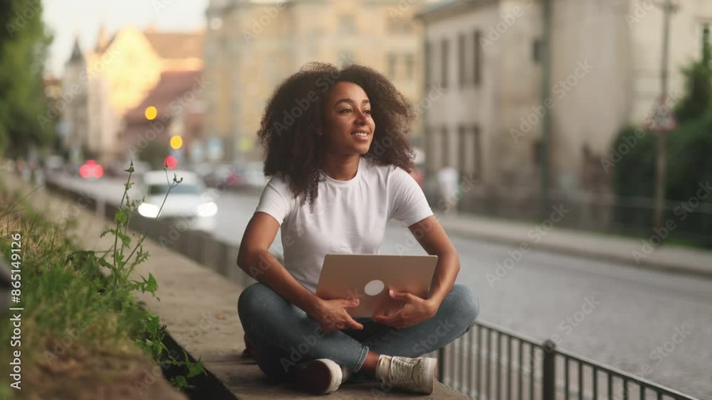 Pretty young african american woman freelancer or student working on laptop at city street Curly girl having distance remote freelance work or education on computer and looking at screen outdoors Pretty young african american woman freelancer or student working on laptop at city street Curly girl having distance remote freelance work or education on computer and looking at screen outdoors