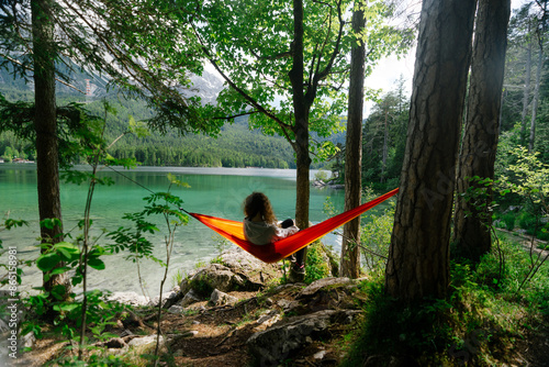 the girl sits in a red hammock on the background of the lake Eibsee