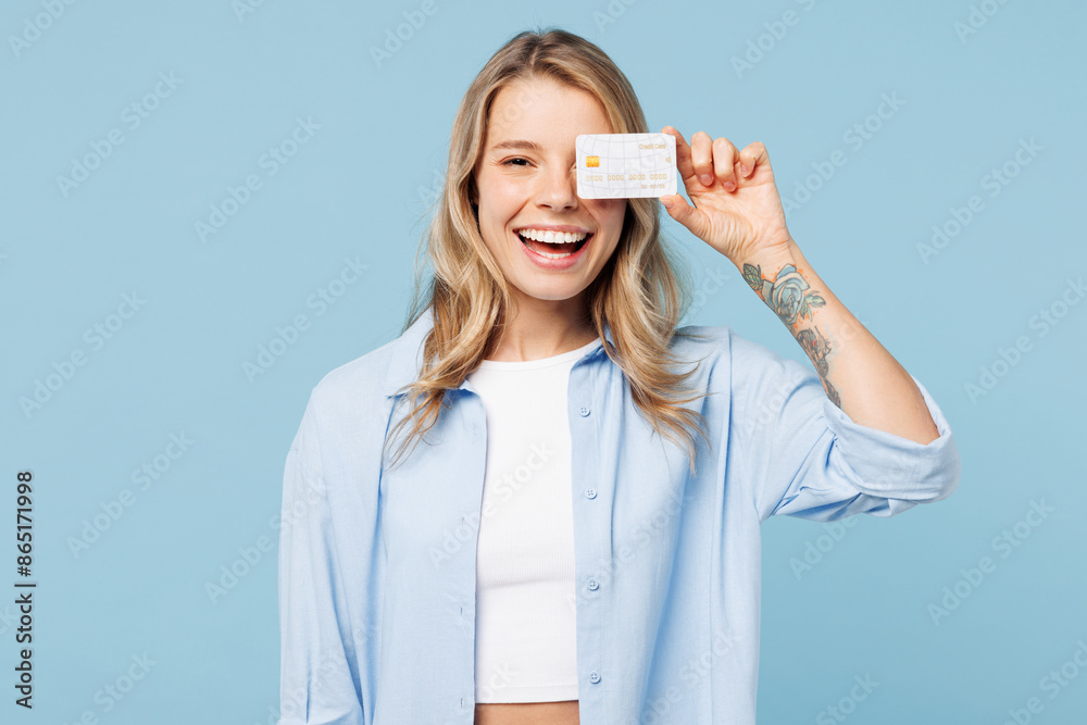 Young happy woman wears white top shirt casual clothes hold in hand cover eye with mock up of credit bank card isolated on plain pastel light blue cyan background studio portrait. Lifestyle concept. Young happy woman wears white top shirt casual clothes hold in hand cover eye with mock up of credit bank card isolated on plain pastel light blue cyan background studio portrait. Lifestyle concept.