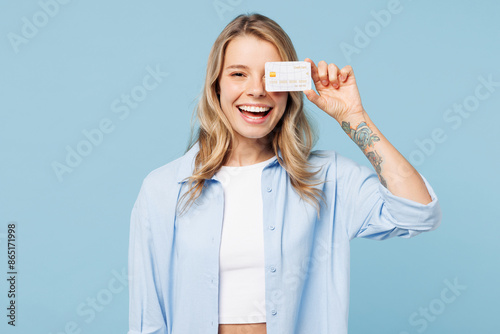Young happy woman wears white top shirt casual clothes hold in hand cover eye with mock up of credit bank card isolated on plain pastel light blue cyan background studio portrait. Lifestyle concept.