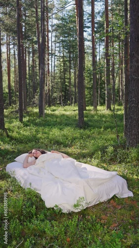 Woman sleeps on a mattress in the summer forest. The girl relaxing in nature. Slow motion, vertical video