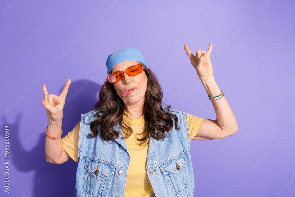 Photo portrait of lovely pensioner lady stick tongue rock horns dressed stylish denim hipster garment isolated on purple color background Photo portrait of lovely pensioner lady stick tongue rock horns dressed stylish denim hipster garment isolated on purple color background