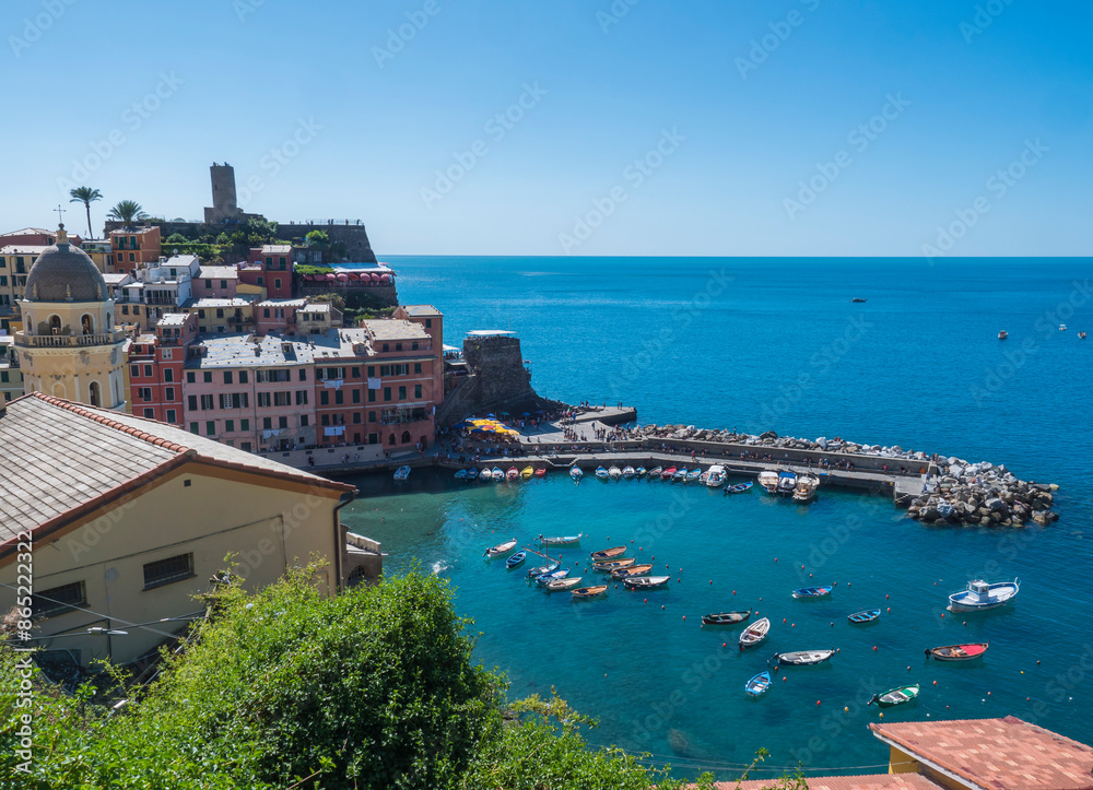 Naklejka premium Picturesque view of Vernazza, with colorful houses, harbor, fishing boats, Vernazza Castle and clear blue sky. Typical traditional village in National park Cinque Terre, Vernazza,, Liguria, Italy