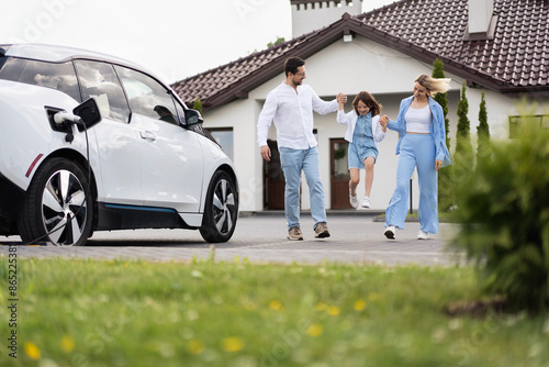 Happy Family Enjoying Time Together Near Electric Car Outside Modern Home