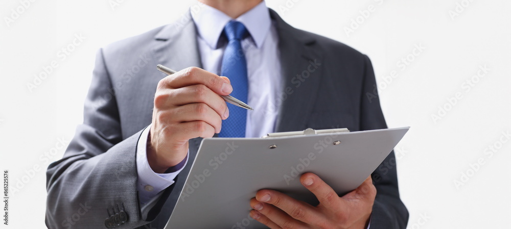 Hand of businessman in suit filling and signing with silver pen partnership agreement form clipped to pad closeup. Management training course some important document team leader ambition concept Hand of businessman in suit filling and signing with silver pen partnership agreement form clipped to pad closeup. Management training course some important document team leader ambition concept