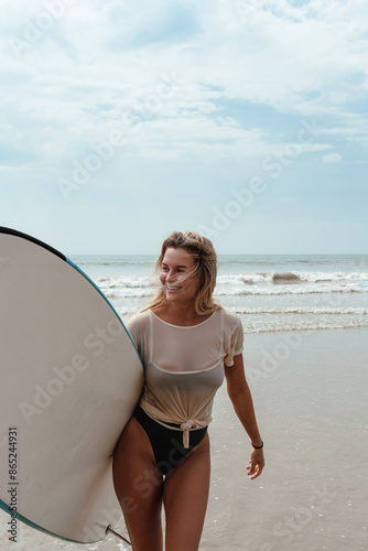 Photography Cheerful woman carries a blue surfboard while walking on the beach