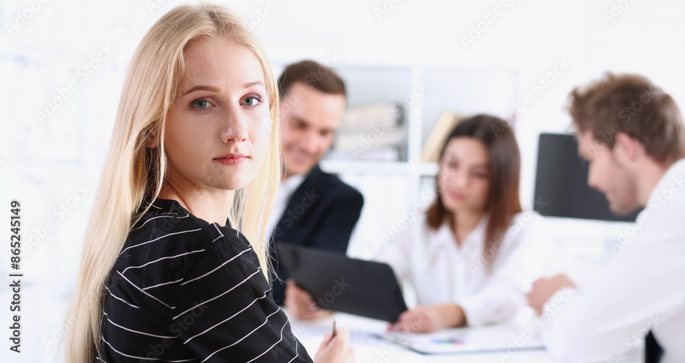 Beautiful smiling cheerful girl at workplace look in camera with colleagues group in background. White collar worker at workspace job offer modern lifestyle client visit profession train concept Beautiful smiling cheerful girl at workplace look in camera with colleagues group in background. White collar worker at workspace job offer modern lifestyle client visit profession train concept