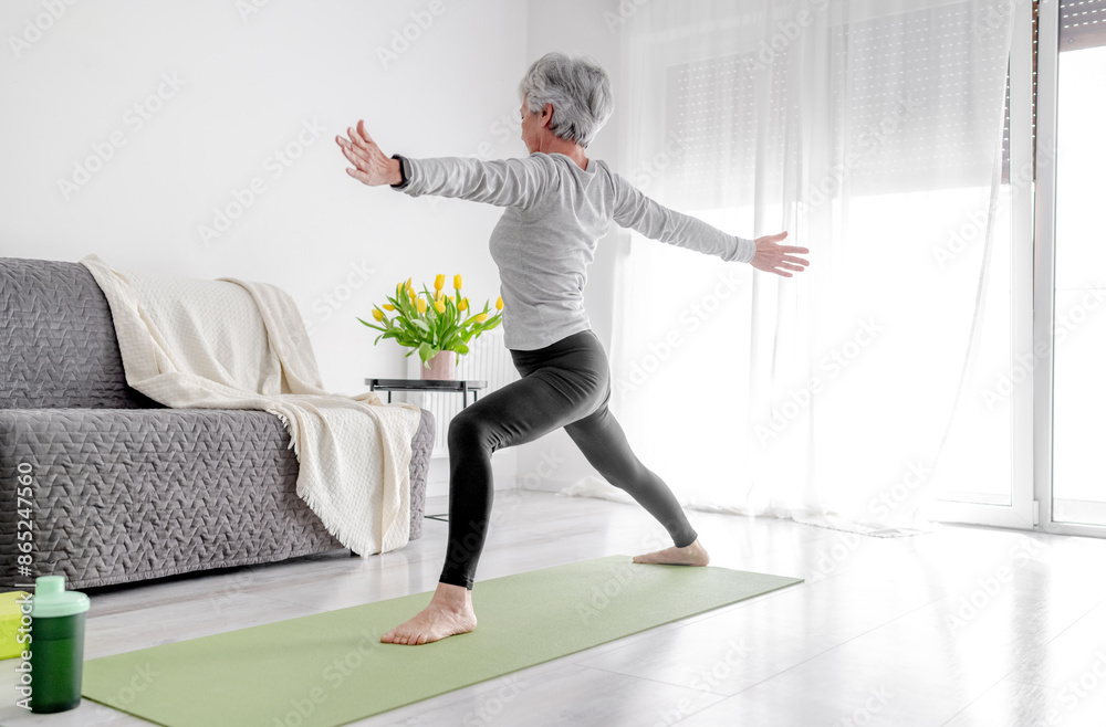 Calm Home Exercises In A Bright Room, A 70-Year-Old Woman Practices Yoga Calm Home Exercises In A Bright Room, A 70-Year-Old Woman Practices Yoga