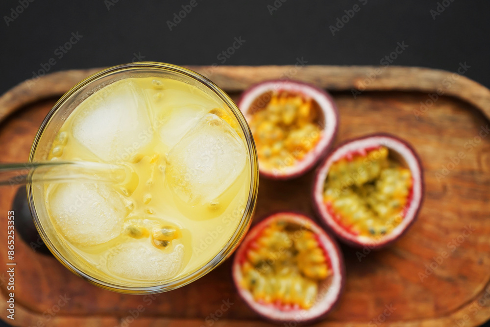 Passion fruits cut in half next to a glass of juice with ice on a wooden tray on a dark background Passion fruits cut in half next to a glass of juice with ice on a wooden tray on a dark background