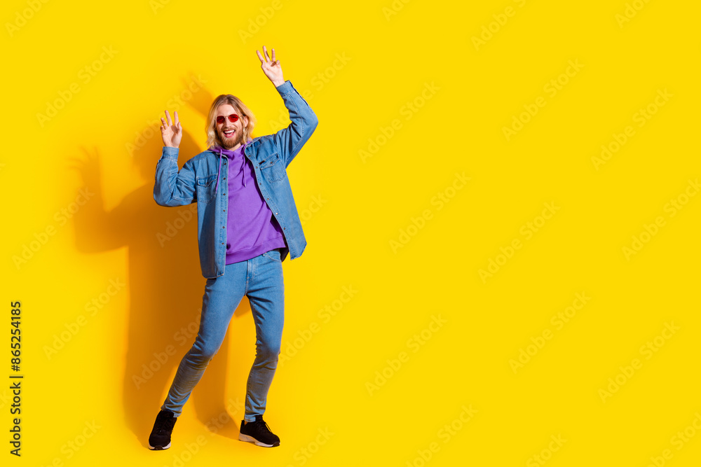 Full body photo of attractive young man sunglass dancing dressed stylish denim clothes isolated on yellow color background Full body photo of attractive young man sunglass dancing dressed stylish denim clothes isolated on yellow color background