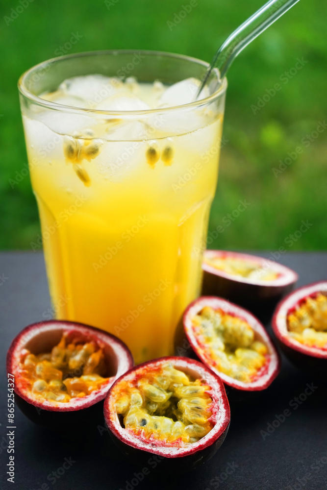 Passion fruits cut in half next to a glass of juice with ice on a background of green grass Passion fruits cut in half next to a glass of juice with ice on a background of green grass