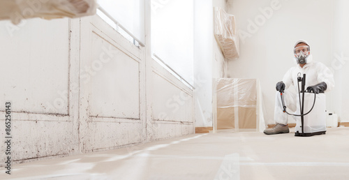 Mold remediation service: Professional worker wearing protective suit, gloves, and respirator mask, holding backpack sprayer at a home renovation site. Equipment to remove mold before house painting photo